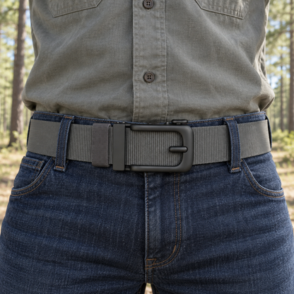 Man draagt de grijze BuckleUp Outdoor Belt door de lussen van een spijkerbroek in een dennenbos