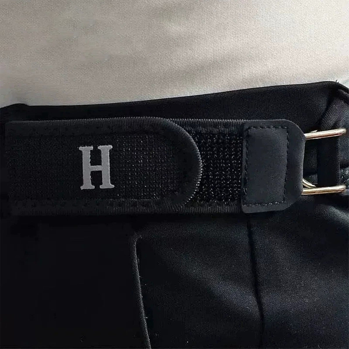 Close-up van de zwarte gesploze riem bevestigd aan een broekband, met klittenband en letter H in detail