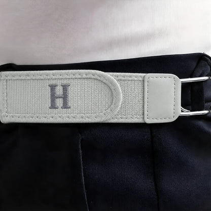 Close-up van de witte BuckleUp gespvrije riemstrap met grijze letter H, bevestigd aan een donkere broekband